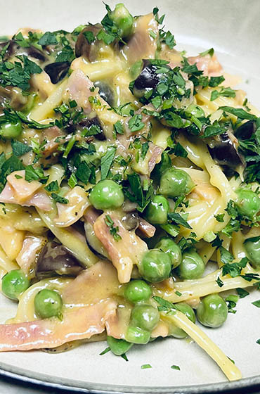 pasta dish topped with meat, peas, and garnish